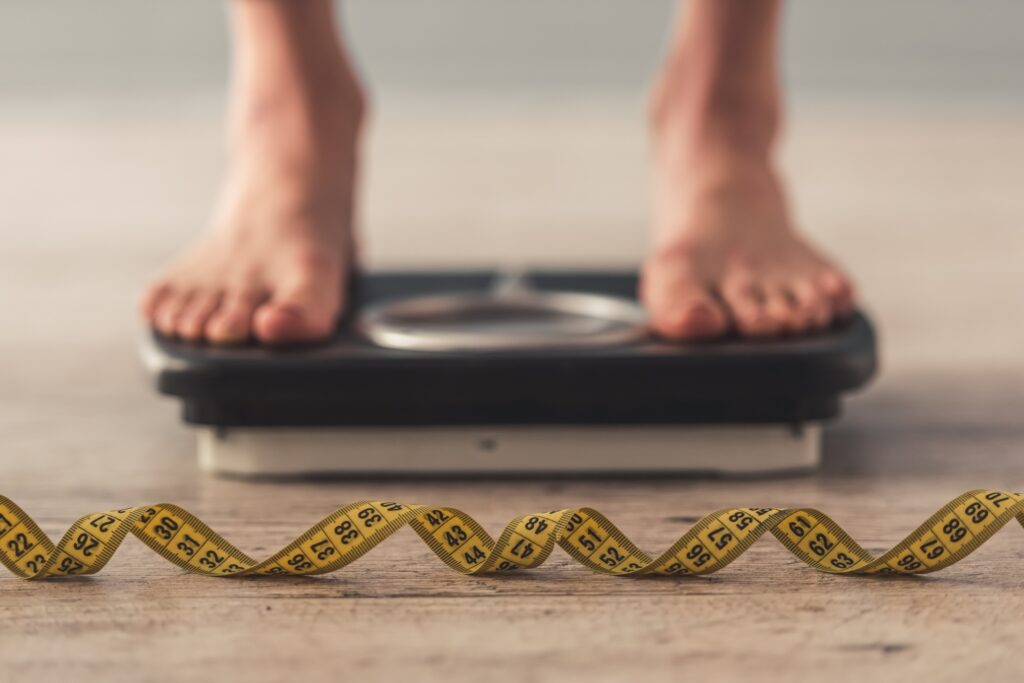 Feet standing on scale with tape measurer curled on the ground.