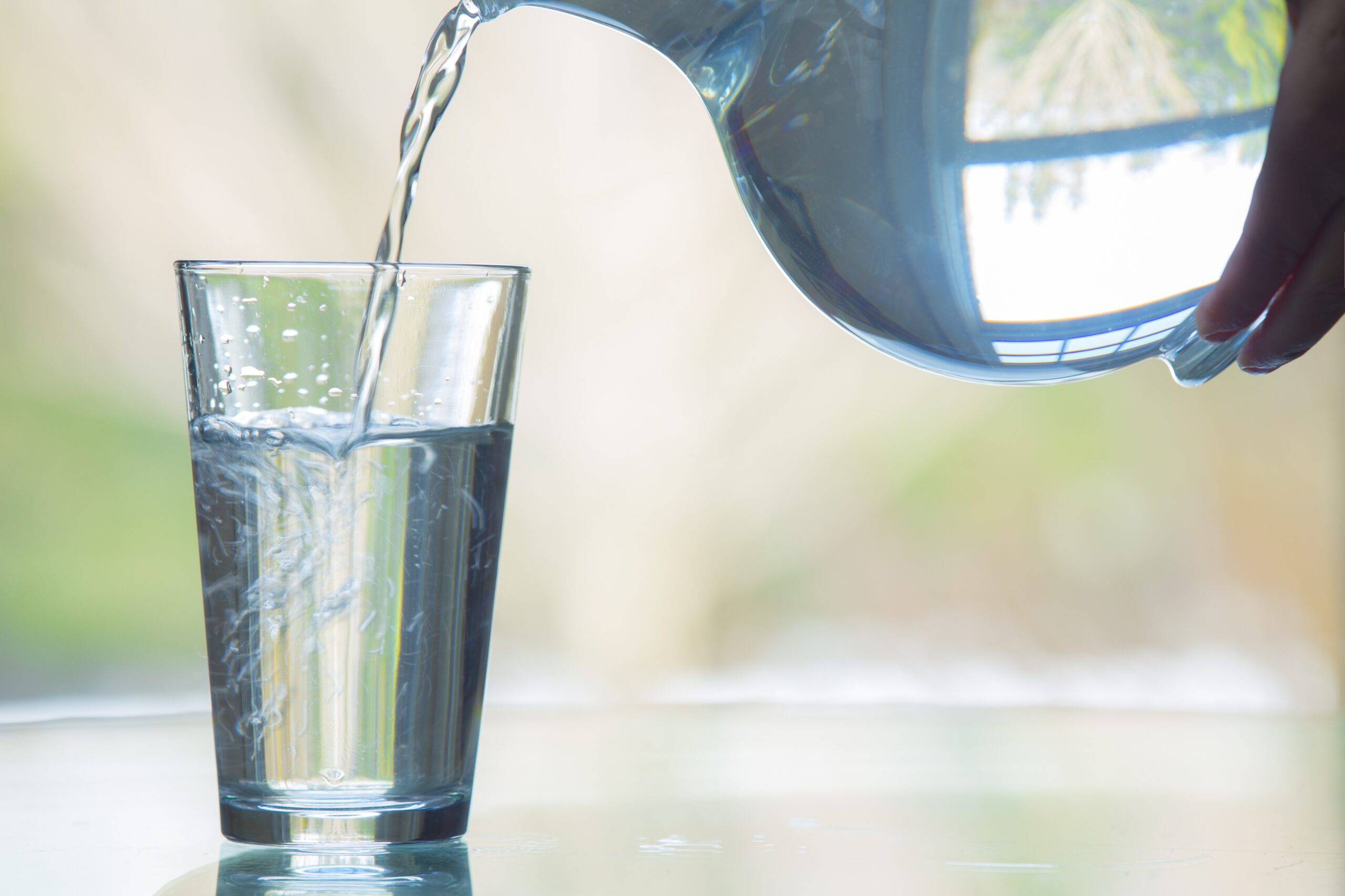 Close-up of person pouring water from a pitcher into a drinking glass on a table.