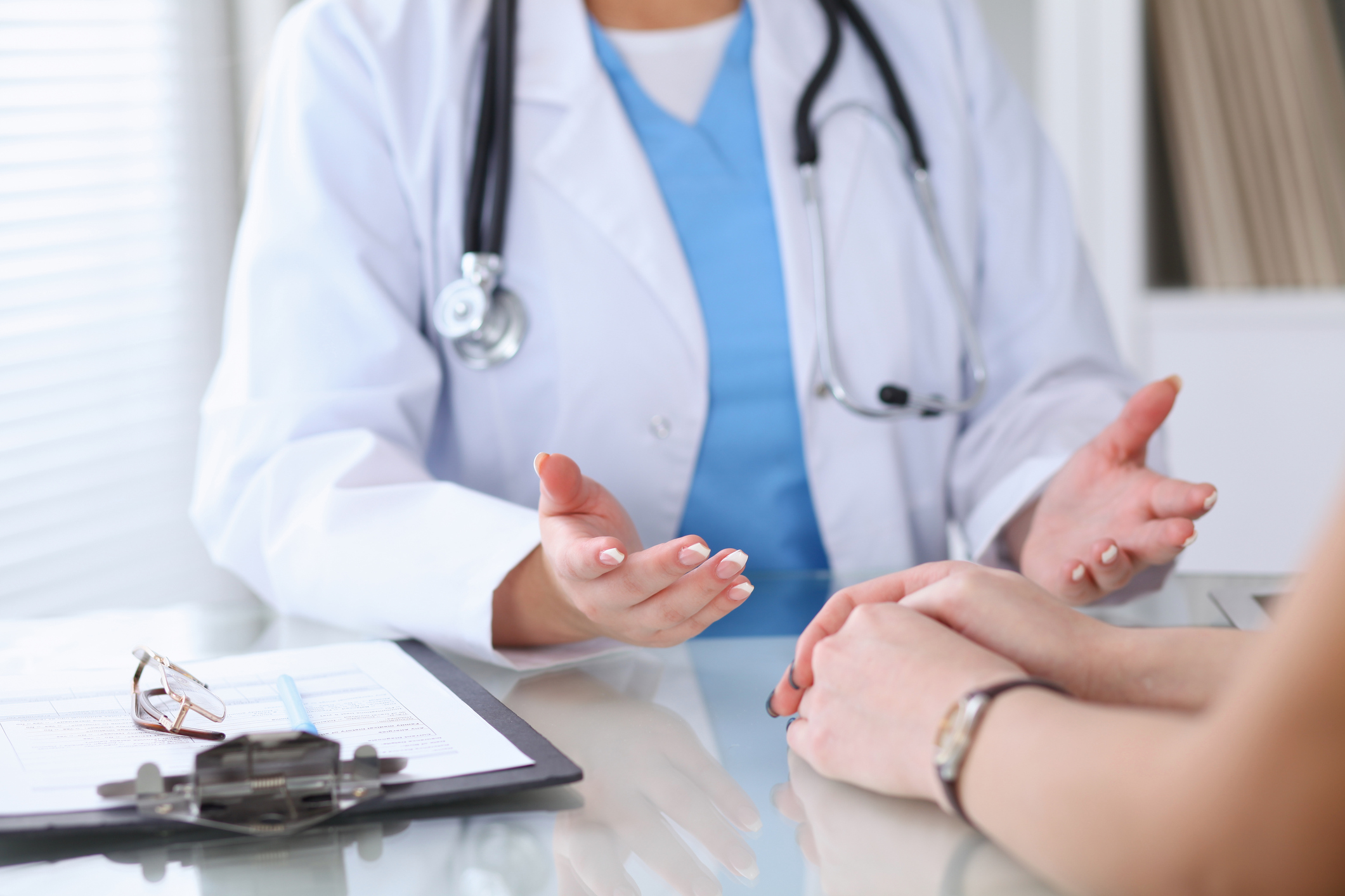 Close-up of female doctor gesturing with hands to the patient on the other side of the desk.