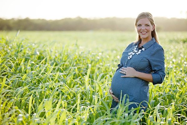 A pregnant woman posing in an open and natural field.