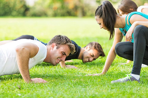 A female coaching two men doing pushups at Fitness in the Park