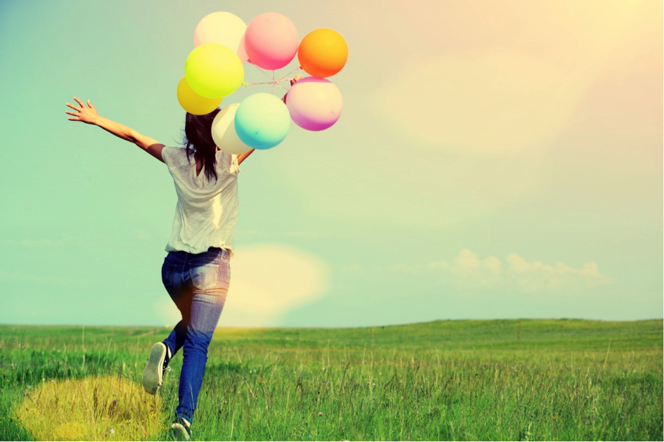 A happy woman in a field with balloons.