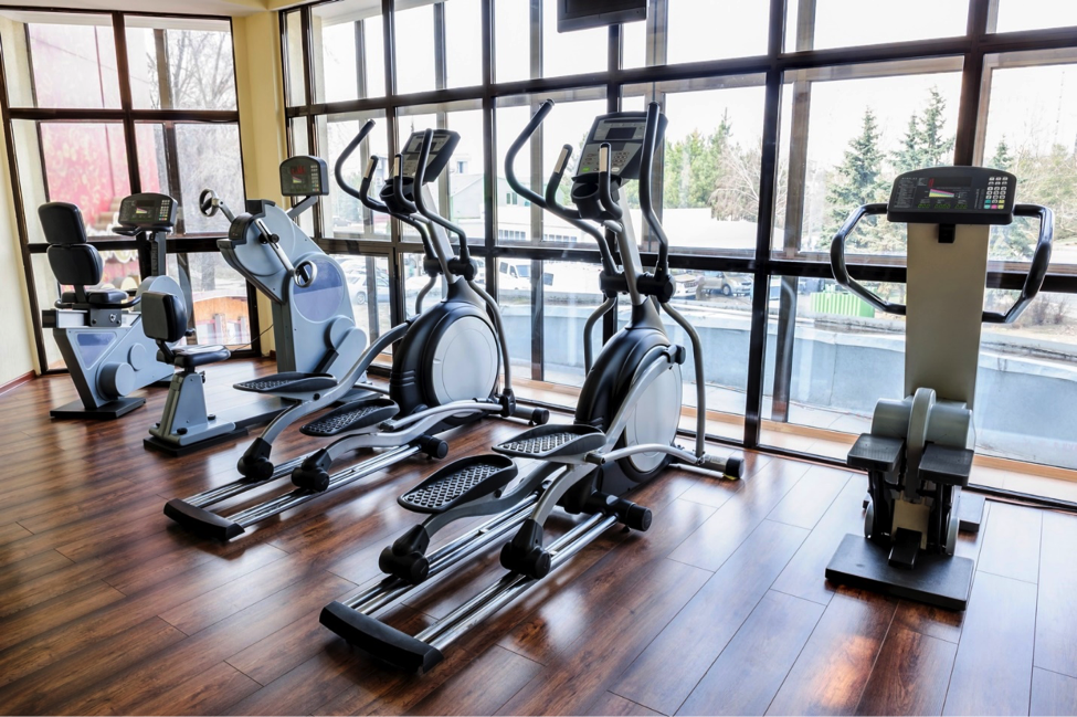 Exercise machines in a row in front of windows.