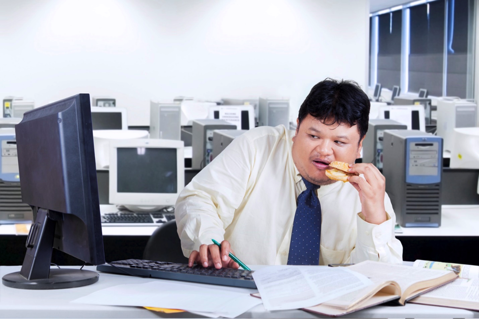 Man sitting in office chair eating while stressed at work