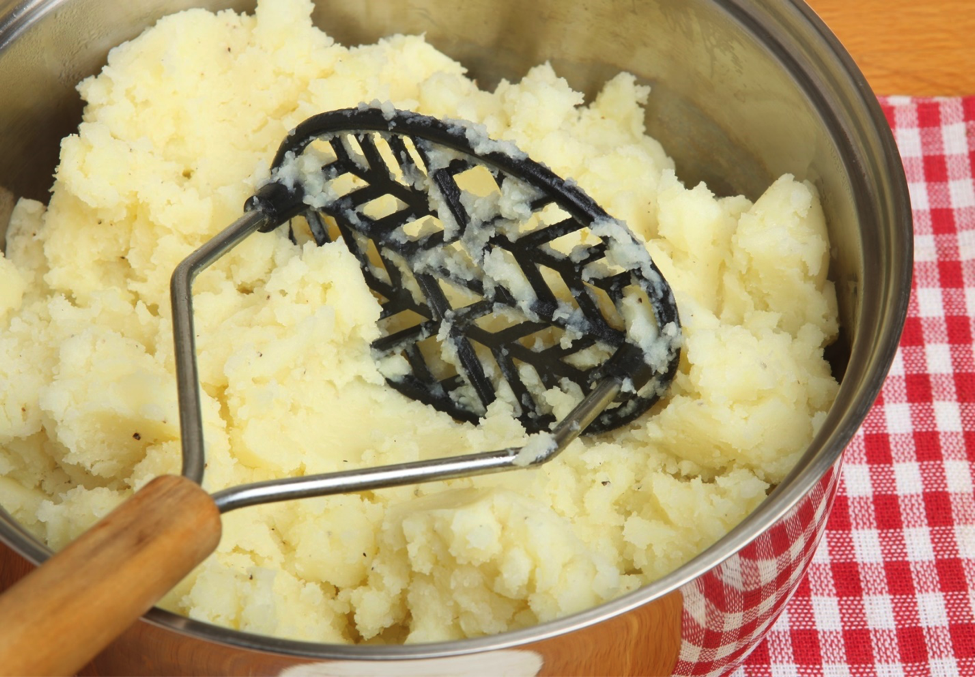 A healthy barbecue option, cauliflower mashed potatoes, in a bowl with masher.