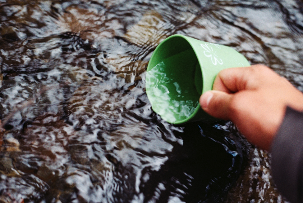 Green cup dipped into a running river.