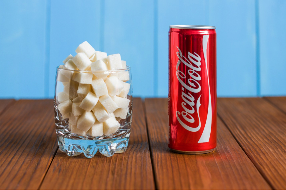 Coca-Cola bottle next to glass of sugar cubes as example of how not to lose weight naturally.