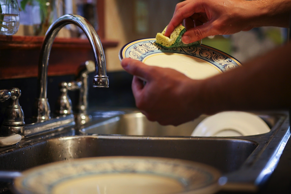 Person cleaning dishes after dinner to avoid late-night snacking.