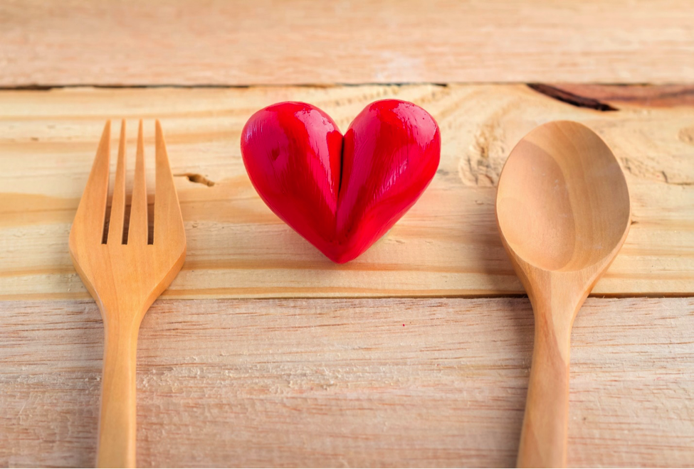 Wooden fork and spoon between wooden heart on a table.