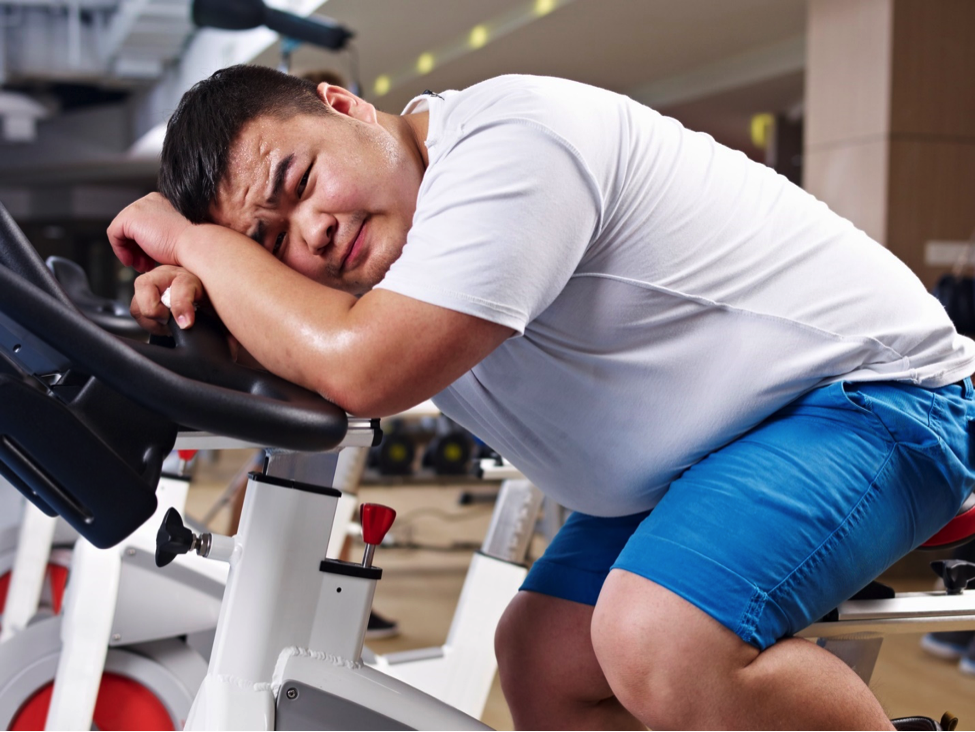 Overweight man tired of working out on fitness bike