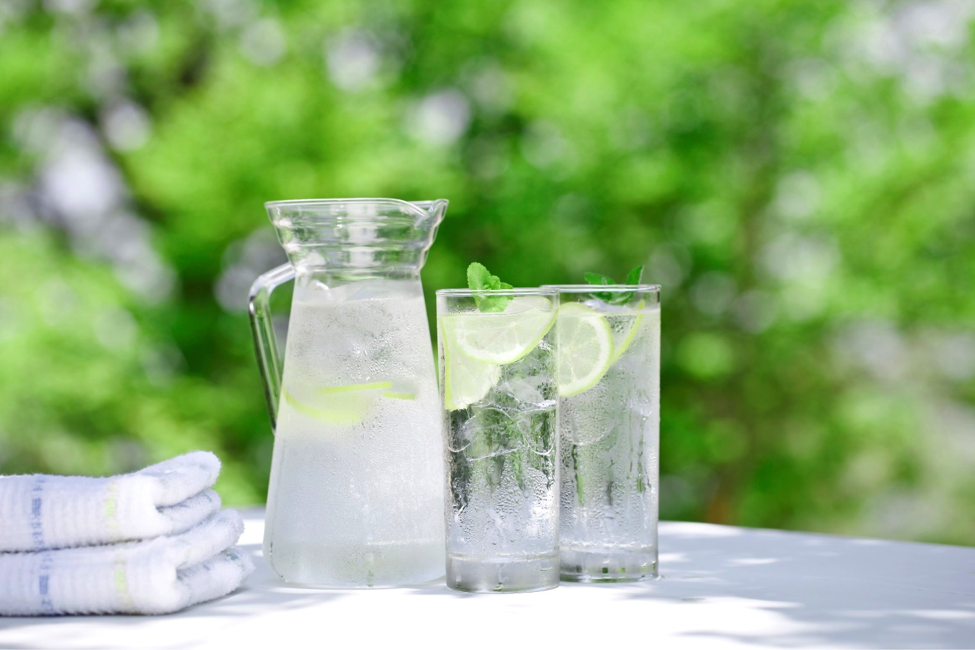Pitcher and glasses of ice cold water on table outside.
