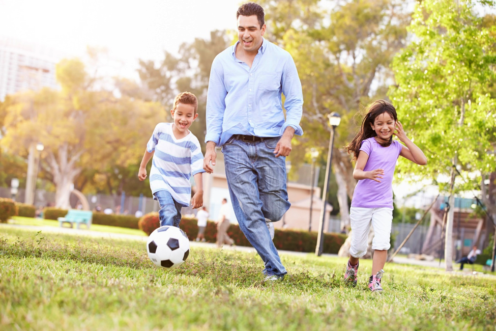 A parent playing soccer with kids for his back-to-school health.