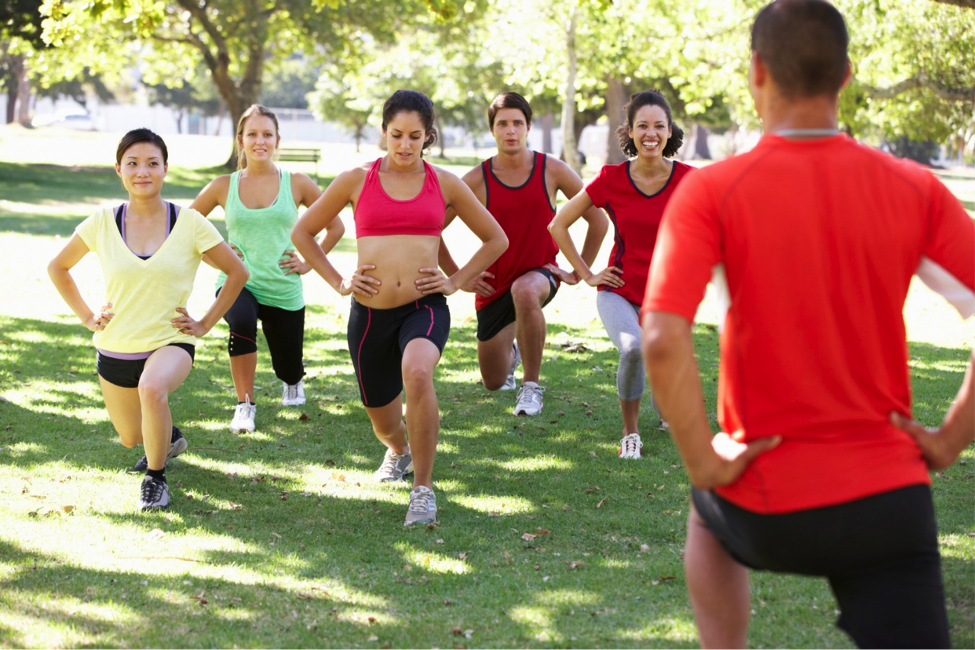 Group of people taking fitness class in park.