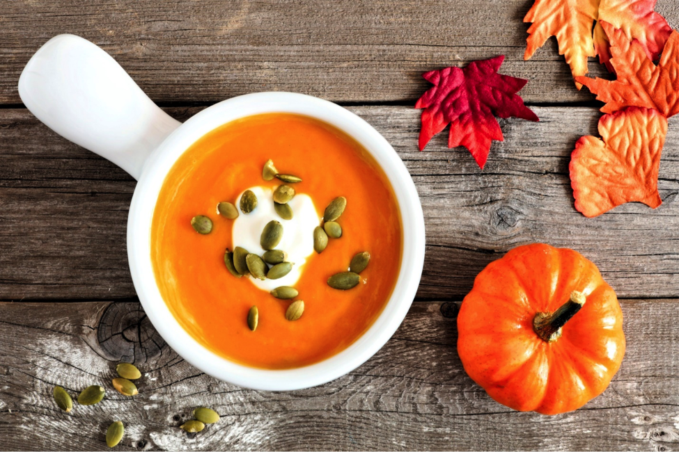 Healthy pumpkin soup in bowl on table with seeds, a pumpkin, and fall leaves