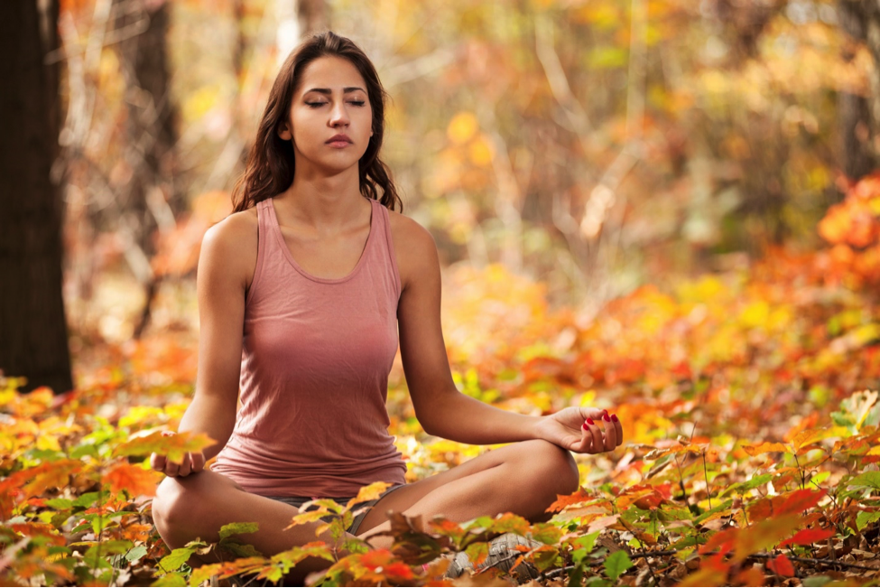 Woman doing yoga pose in autumn leaves as one of the best outdoor fitness ideas.