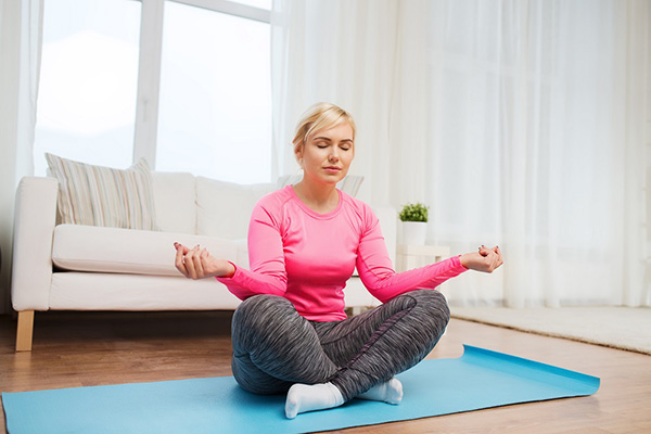 A woman meditating in her living room to gain a healthy body image