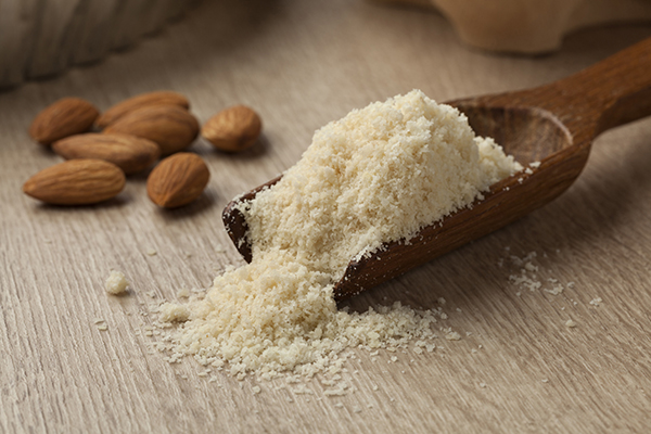 Wooden spoon spilling almond flour near almonds for cooking substitutions