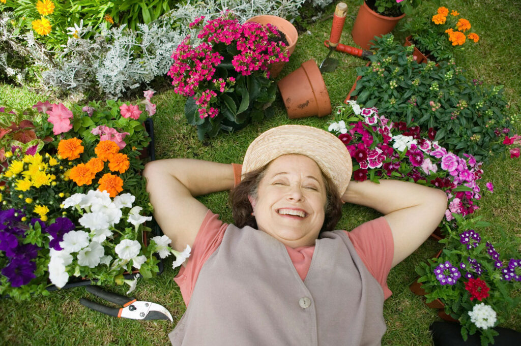 Happy older woman lying down surrounded by gardening tools and plants.