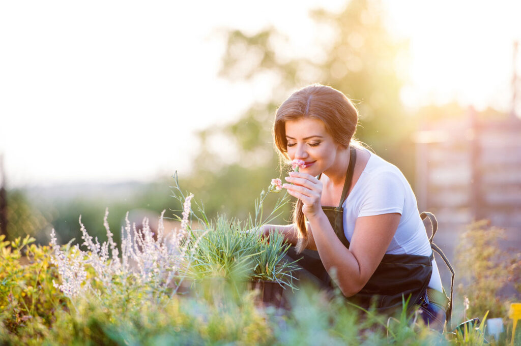 Woman smiling and closing eyes as she smells flowers in a garden.