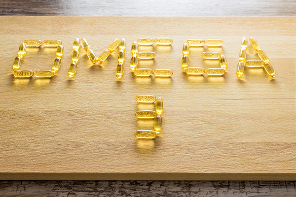 The words, Omega 3, written in yellow, gel vitamin pills on cutting board.