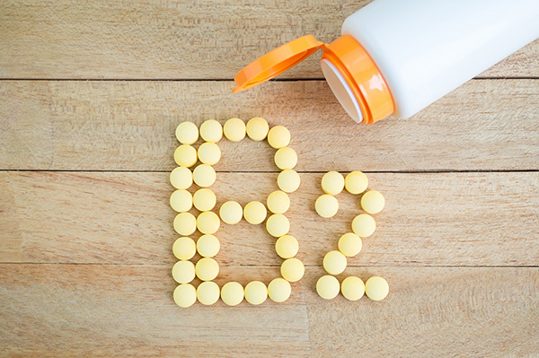 Vitamin bottle open with pills spelling ‘B2’ against wood.