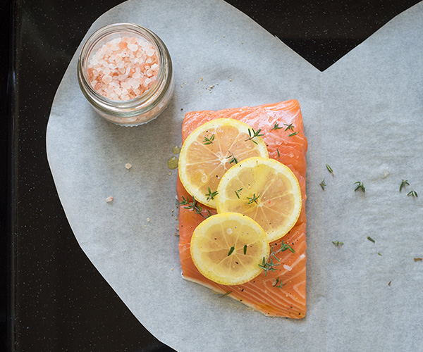 Small slice of salmon with lemon wedges on top and a cutout heart background.