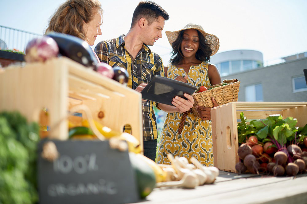 Three young adults choosing healthy spring food items at a farmer’s market.