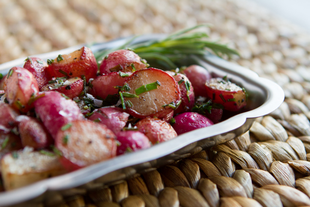 Roasted radishes and herbs in a silver platter placed on a tablemat.