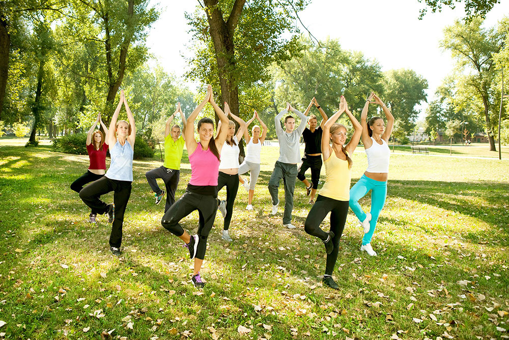 Group of people doing stand-up positions in a park for their San Antonio yoga class.
