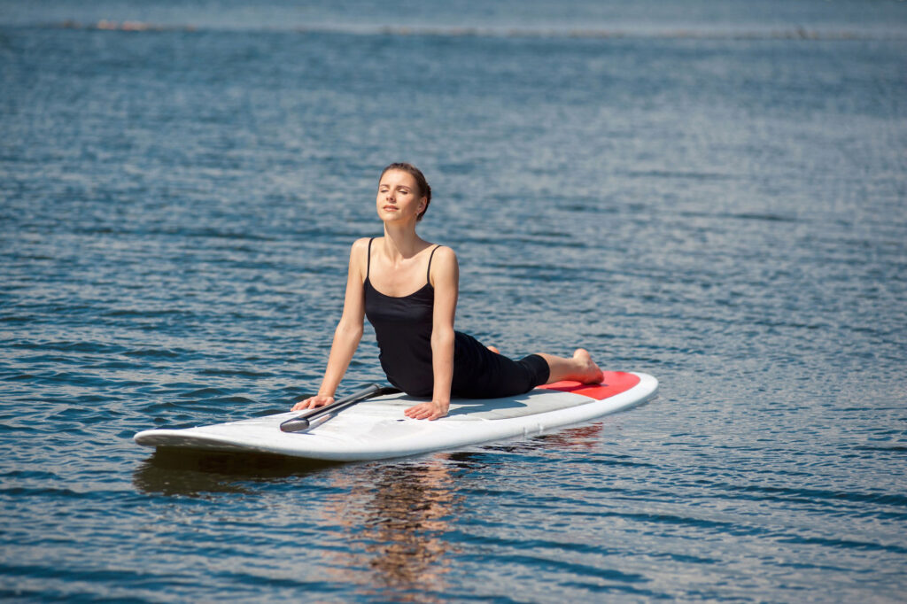 Woman doing yoga position on stand up paddleboard in water for San Antonio yoga class.