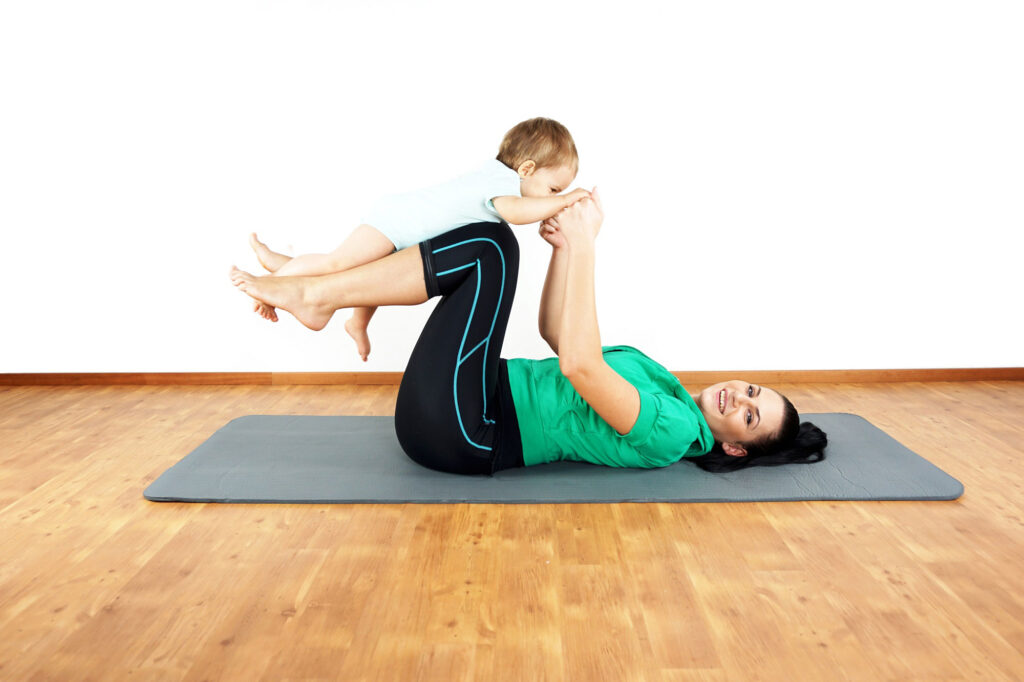 Woman lying on yoga mat with legs in the air while holding baby at San Antonio yoga class.
