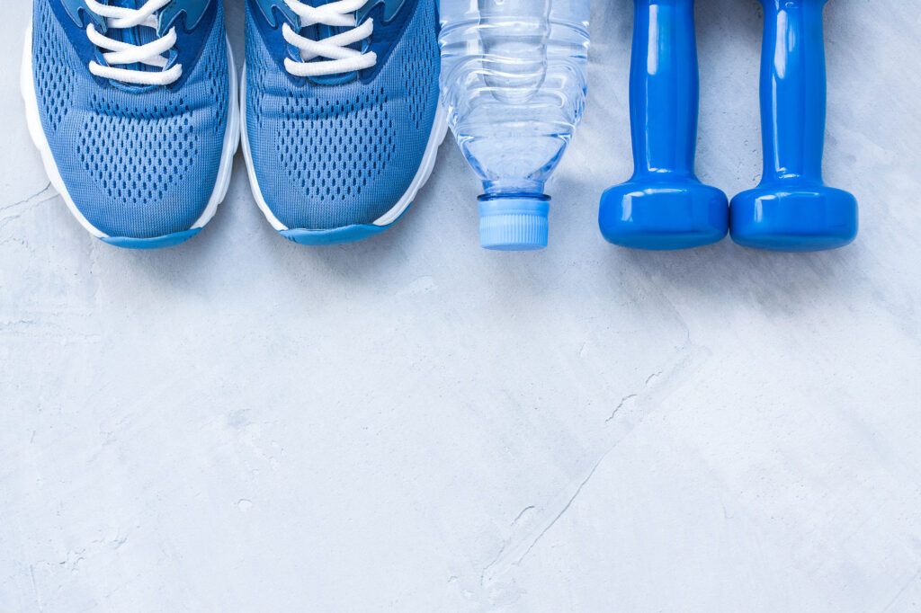 Blue tennis shoes, water bottle, and small dumbbells in a line on concrete.