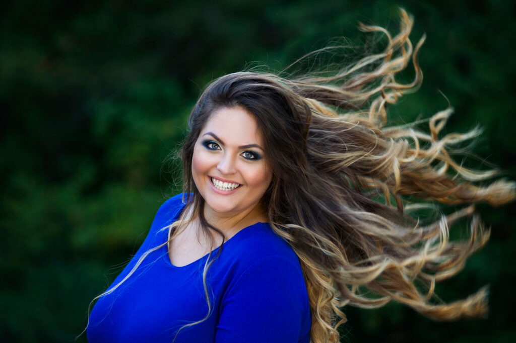 size woman confidently smiling while her long curly hair blows in the wind.