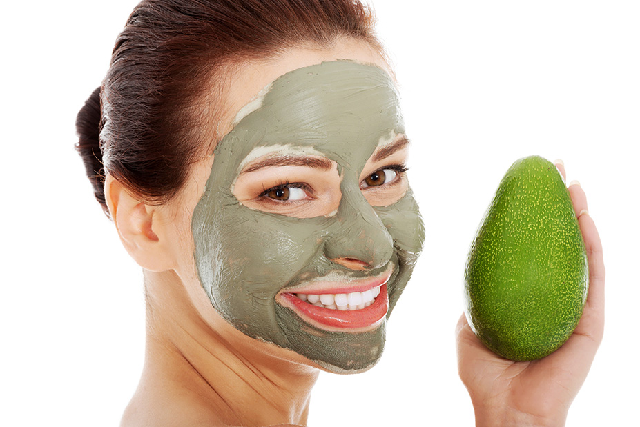 Woman with avocado face mask smiling and holding avocado.