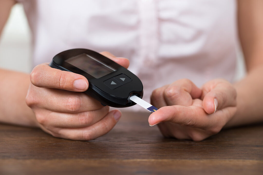 Close up of person taking blood sugar level with finger and insulin device.