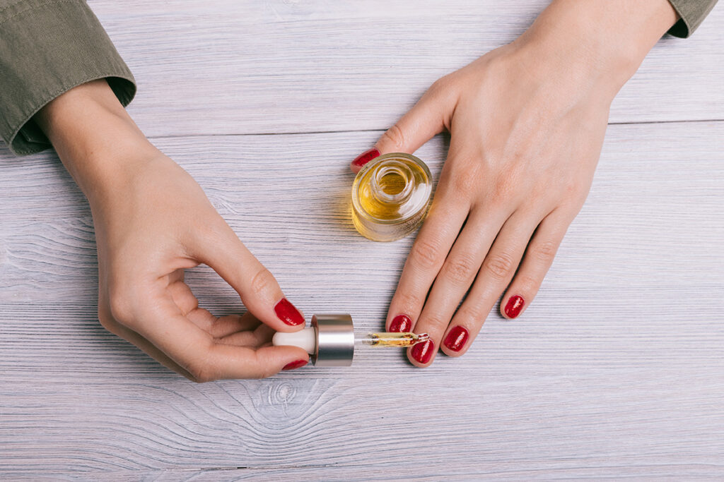 Close up of woman dripping avocado oil onto red-painted finger nails.