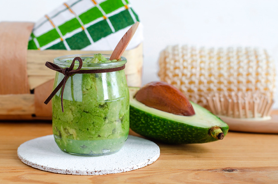 Avocado scrub in clear jar next to avocado half with spa kit in the background.