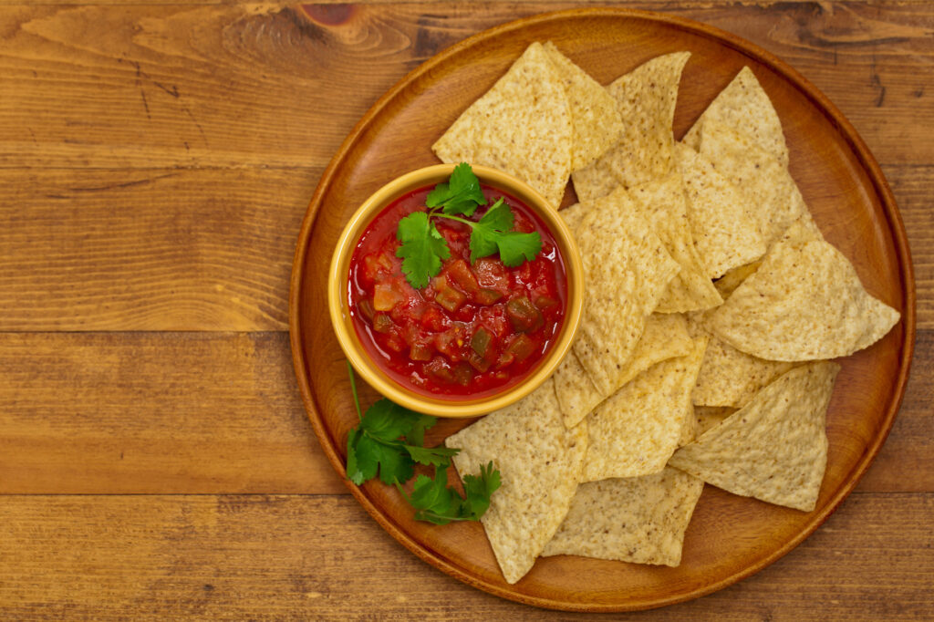 Tray of tortilla chips and bowl of salsa on wooden table.