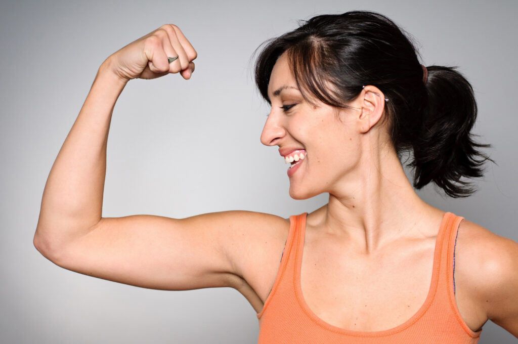 Woman smiling and looking at arm while flexing to represent vitamin D health benefits.
