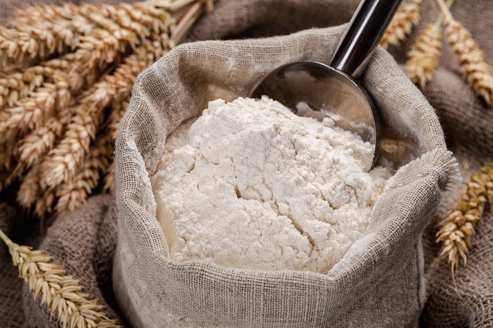 Strands of wheat placed around bag of flour with wooden scooper.