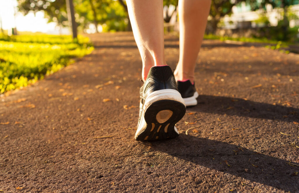 Close up of woman’s ankles and shoes while walking down a park path.
