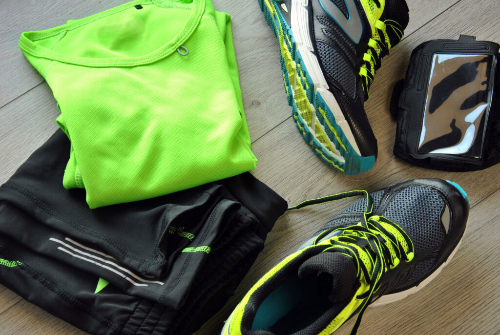 Green athletic shirt, black athletic shorts, tennis shoes, and phone cover laid out.