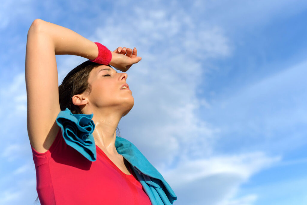 Woman putting hand to forehead with towel around neck and blue sky in the background.
