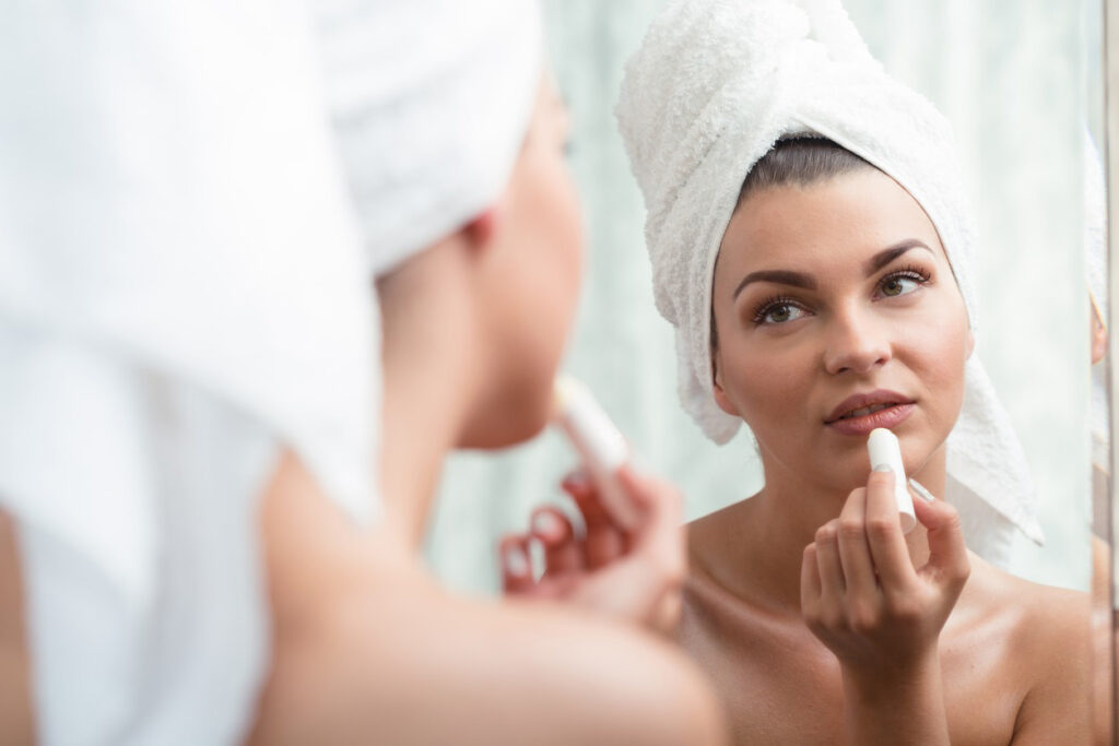 Woman applying lip balm after shower to follow summer skin care tips.