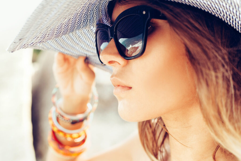 Woman touching hat on her head and wearing sunglasses to follow summer skin care tips.