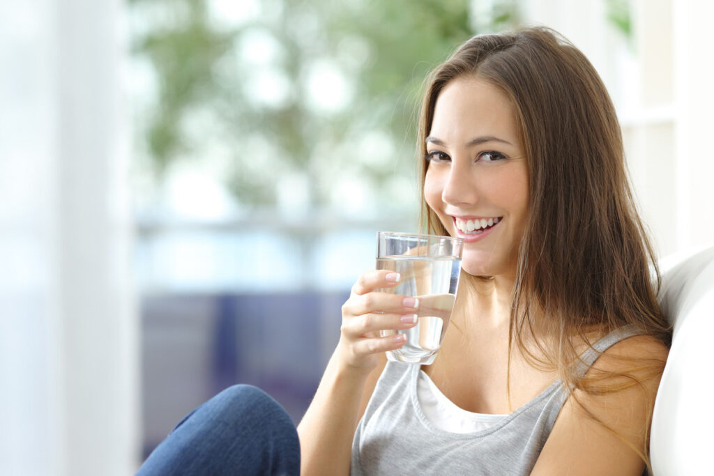 Woman smiling while holding a clear glass of water.