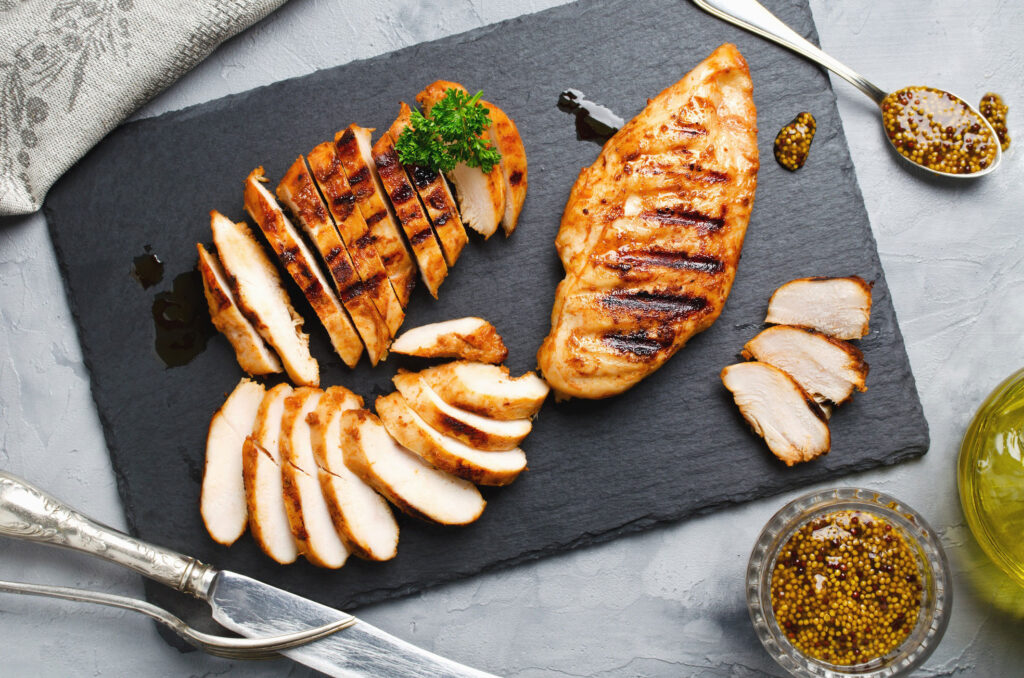 Sliced, grilled chicken on a black cutting board.