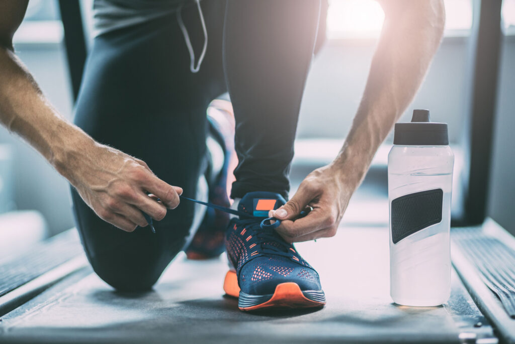 Man bending to tie shoe next to water bottle.