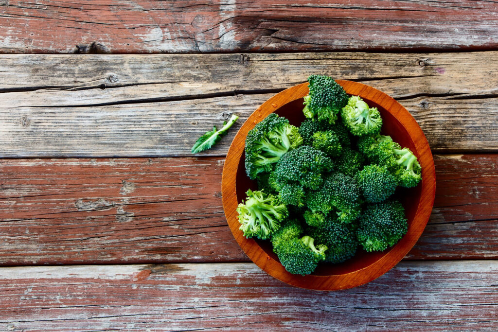 Broccoli in a bowl sitting on a wooden table.