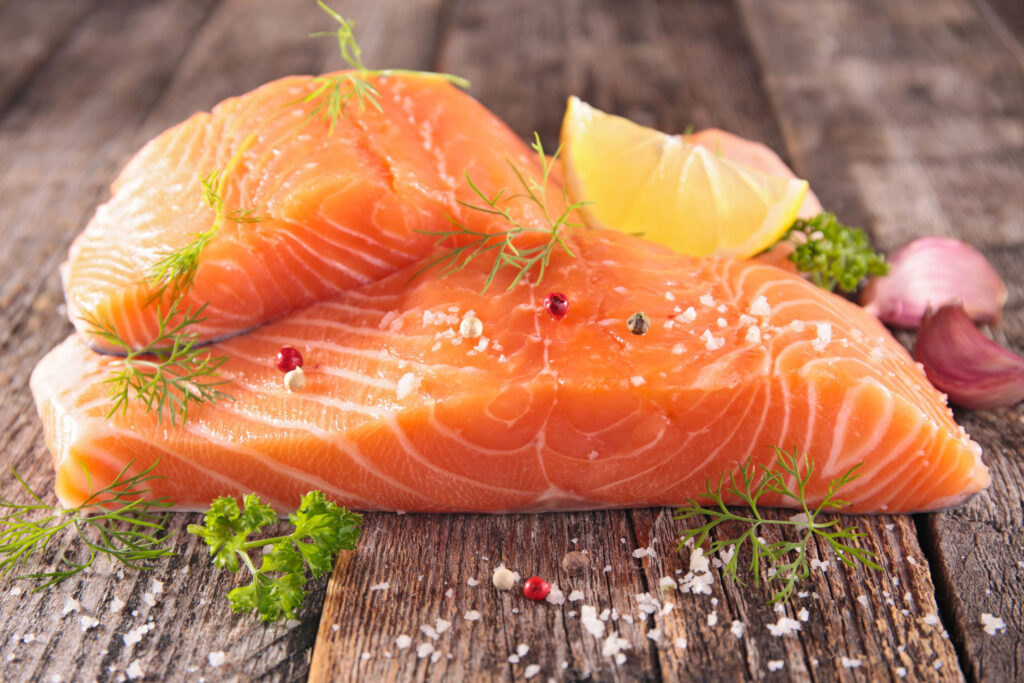 Raw salmon sprinkled with rosemary and salt on top of a wooden table.